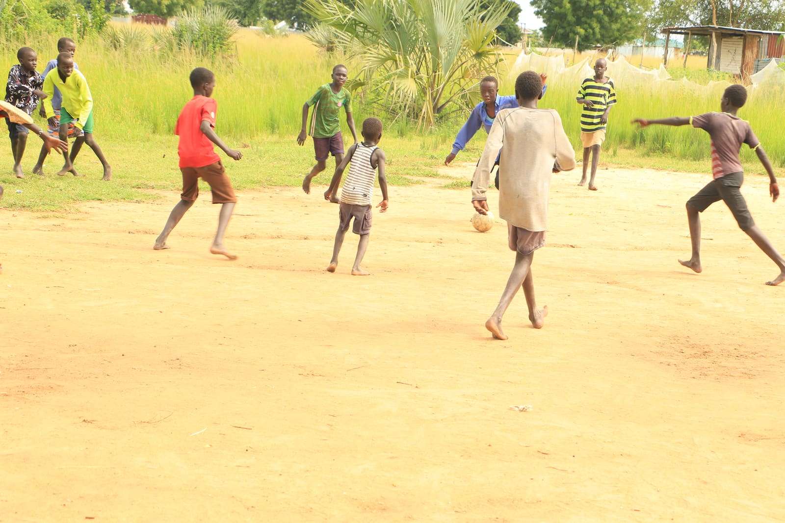 Children running after the ball on a sandy pitch