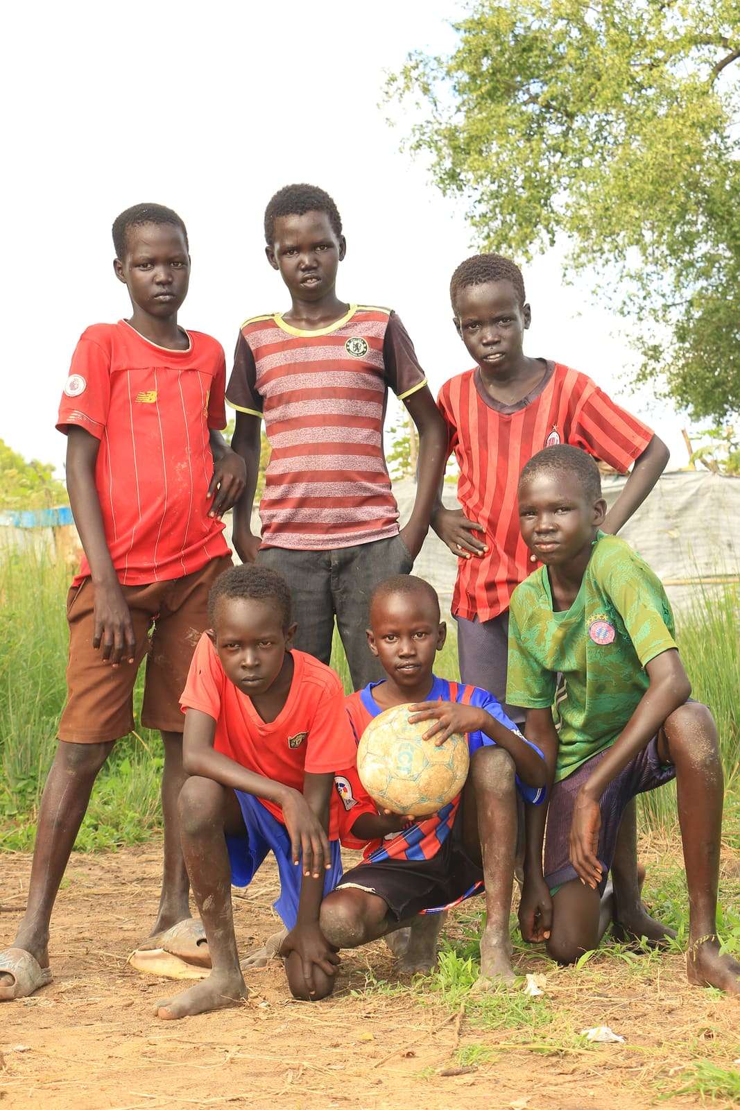 Six boys in football shirts, three standing and three kneeling around a ball