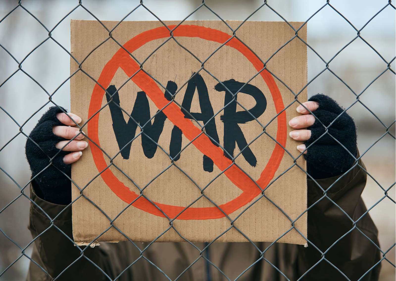 A hand-made “No war” sign held against a wire fence